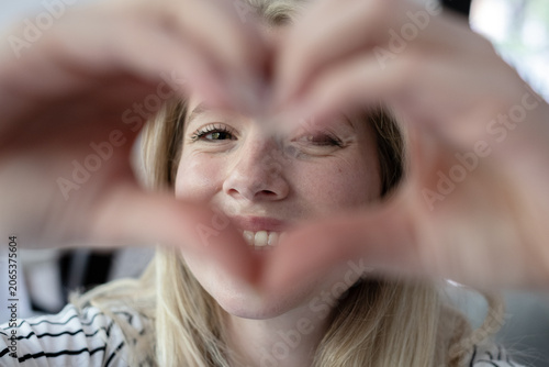 Obraz na plátne Smiling young adult woman forming a heart gesture with her fingers, showing genu