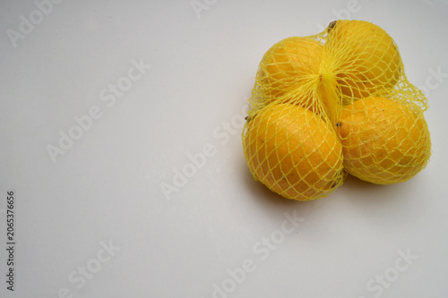 yellow lemon in a yellow mesh  on a white background corner composition horizontal layout, lemons close up with generous copy space,