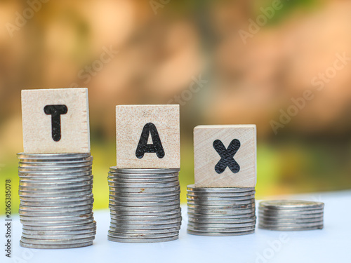Wooden blocks with the word TAX on stacked coins, financial concept of tax growth, savings, and economic burden.