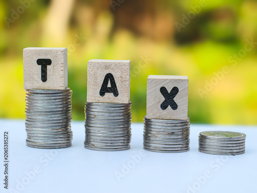 Wooden blocks with the word TAX on stacked coins, financial concept of tax growth, savings, and economic burden.
