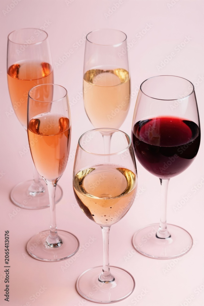 Fototapeta premium Assorted wine and champagne glasses with sparkling rose white and red wine. Drinks stand on pink background. Elegant variety of bubbly beverages for festive celebrations.