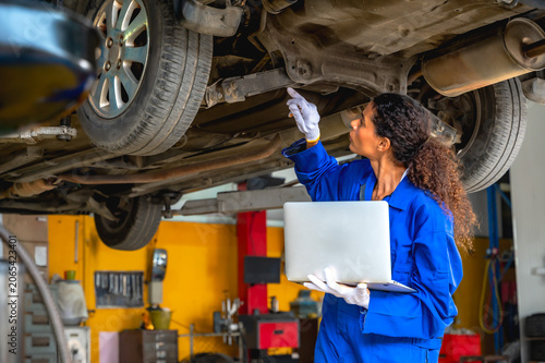 Auto mechanic woman using tool examining vehicle chassis and suspension to diagnose mechanical problems in auto repair service station