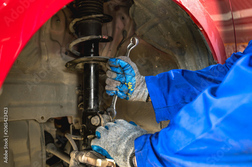 Close up unrecognized car mechanic working on vehicle suspension system, repairing and assembling a coil spring onto a shock absorber strut inside auto repair shop garage