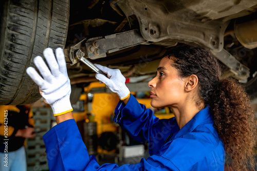 Female auto mechanic using tool examining vehicle chassis and suspension to diagnose mechanical problems in auto repair service station