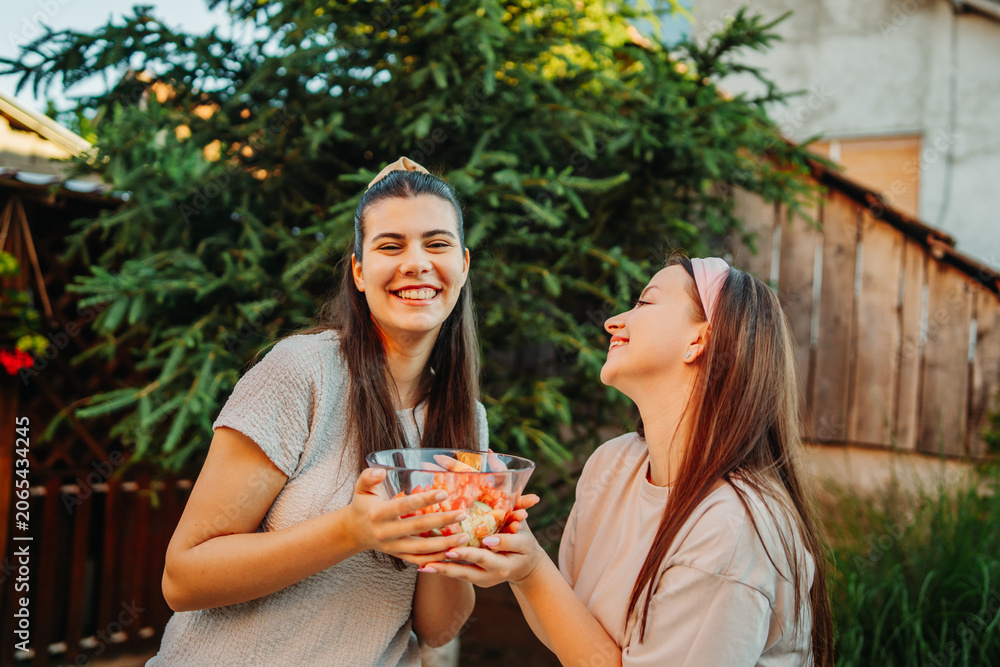 Fototapeta premium Young women sharing fruit salad, enjoying healthy summer friendship