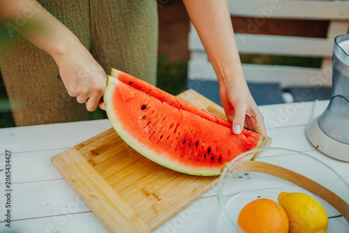 Woman slicing fresh watermelon on cutting board outdoors