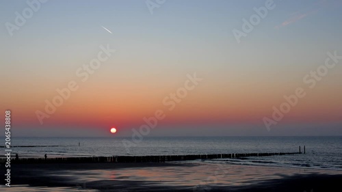 Cinematic sunset over the North Sea at Cadzand beach with wooden breakwaters and contrail in sky