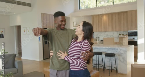 Diverse couple embracing, man holding keys, showing move-in joy with boxes in open-plan home