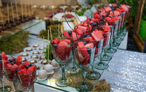 Elegant catering display with fresh watermelon and blueberries served in glass cups at a festive buffet table. Healthy dessert concept for events, weddings and hospitality