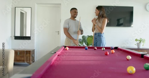 African couple holding cues behind red pool table, glancing at scattered balls and planning shot