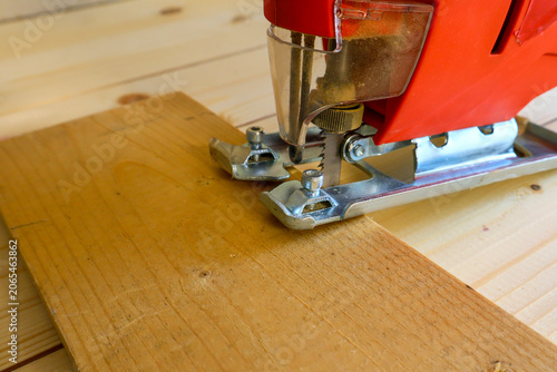 Red jigsaw rests on light wooden plank, metal base plate pressed to surface. Blade alignment and wood grain texture highlight preparation for accurate cut.