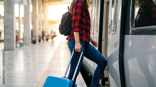 Young woman traveler boarding a passenger train with a blue suitcase at the station platform