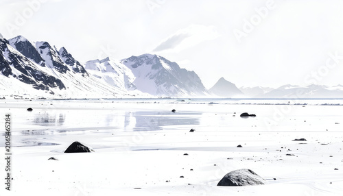 Snowy mountains meet a frozen sea with scattered rocks on a bright, hazy, winter day