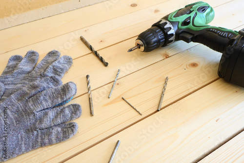 Cordless drill with green accents lies beside scattered drill bits. Gray knitted work glove signals safety and readiness for hands-on work