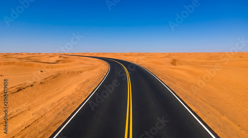 Asphalt road winding through golden sand dunes in desert landscape under clear blue sky background