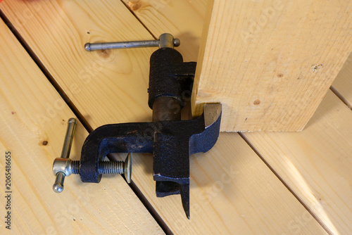 Sturdy black clamp grips light pine boards at a tight corner joint. Ready-for-work workshop vibe with focus on carpentry precision.