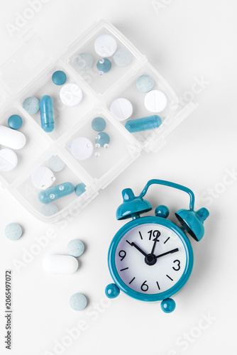 Top view of pill organizer and alarm clock on white background, Daily medication and supplement routine concept