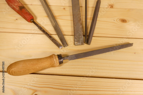 Assorted metal rasps and files with wooden and plastic handles rest on warm pine planks. Classic workshop tools evoke craftsmanship and tactile, deliberate work.