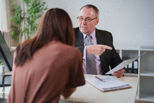 Foto Furious senior boss pointing finger and holding document, reprimanding young fem