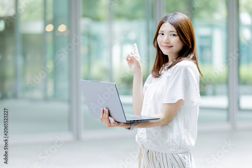 ノートパソコンを持ちながら指差しをする日本人女性