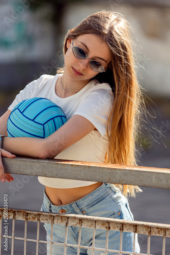 Outdoor portrait of a blonde pre-teen girl wearing bright blue sunglasses and holding a matching blue ball
