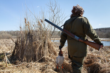 A hunter with a shot drake stands near the duck blind