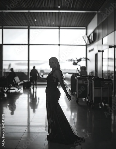 Elegant Woman in Flowing Gown Standing in Backlit Airport Terminal