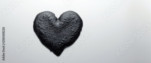 Shiny bitumen blot in heart shape on smooth white surface
