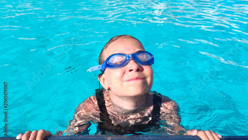 Young girl wearing swimming goggles in a clear blue pool on a sunny summer day. Perfect for themes of childhood, swimming lessons, family vacations, water sports, and healthy outdoor activities.