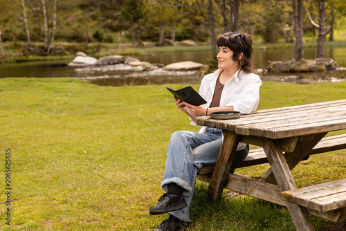 Woman sits on a wooden picnic bench, reading a book