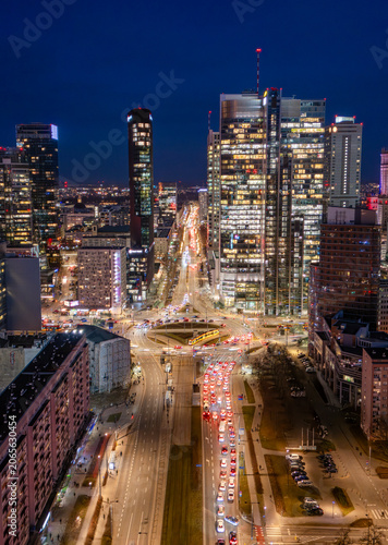 Aerial view of the illuminated skyscrapers and busy urban traffic at the Rondo ONZ roundabout in the city center of Warsaw at night, Poland.