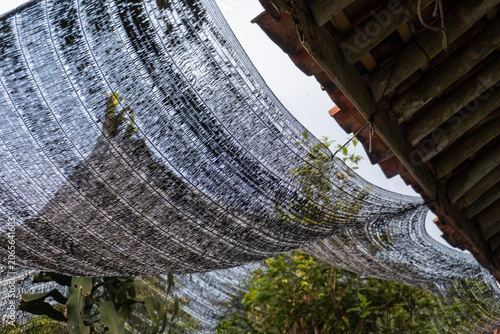 Black Woven Shade Net Hanging Below A Tiled Roof