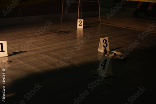 Forensic evidence markers and a bloody knife document the floor of a crime scene cordoned with yellow police tape during investigation.