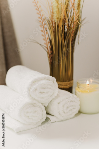 Minimalist still life of luxury spa essentials. White cotton towels with candle on a table.