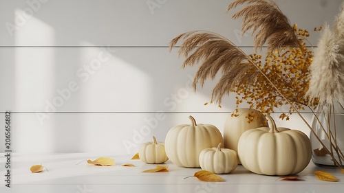 Arrangement of light colored pumpkins and dried grasses with autumn leaves scattered on a white wooden surface