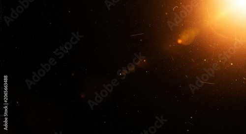 A dark background is illuminated by a bright, warm light source, creating a scattering of golden sparks and streaks.