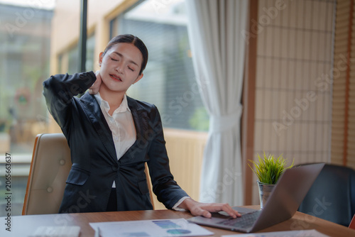 Foto Asian businesswoman working on her laptop in an office, holding her neck in pain