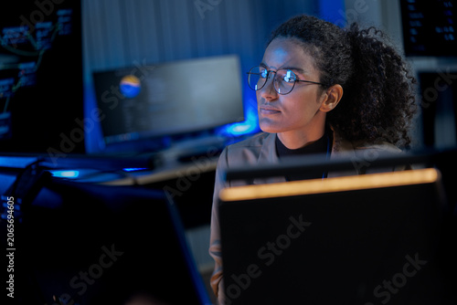 Black female cybersecurity expert examines data visualizations on a holographic-style display in a dark AI innovation lab.