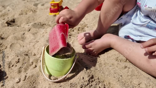 Child pouring sand into bucket on beach close up toddler playing in sandbox summer outdoor activity