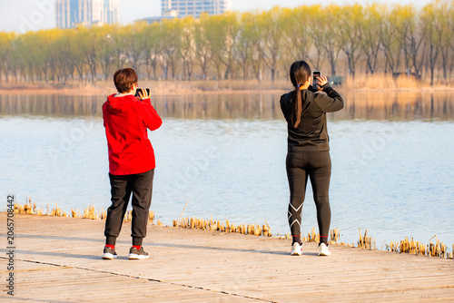 People walking and taking photos on riverside boardwalk in vibrant spring park