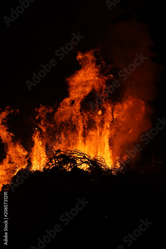 A massive traditional Judas burning bonfire lights up the night sky and a gathered crowd in Crete, Greece. Authentic Orthodox Easter cultural celebration at night.