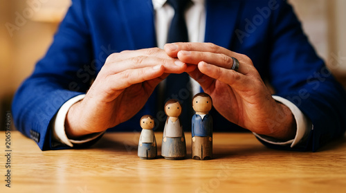 Man in blue suit protecting wooden family figures with hands on table image
