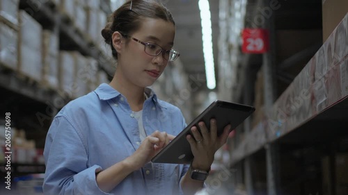 Female Inventory Controller Using Tablet in Warehouse Aisle. Digital inventory, warehouse technology, stock management