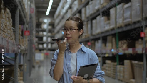 Female Warehouse Employee Communicating by Phone During Inventory Operations. Logistics communication, warehouse coordination, supply chain management