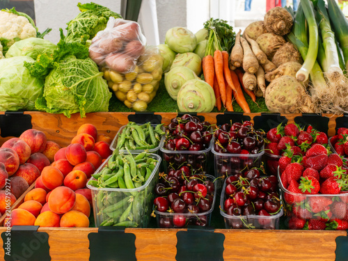 Market stand filled with strawberries, sweet cherries, apricots, sugar snap peas, cabbage, savoy cabbage, kohlrabi, carrot, celeriac, leek and cauliflower. Colorful seasonal food selection for grocery