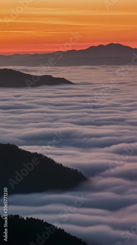Cinematic aerial view of ethereal sea of clouds at sunrise with silhouetted mountain ranges below, symbolizing serenity, vastness, and a new beginning