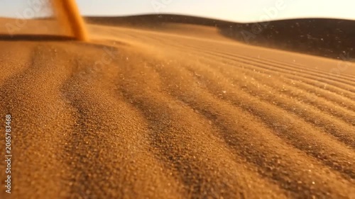 Extreme close up of golden sand dunes in a desert with wind blowing fine sand particles creating ripples and patterns on the surface under a clear sky