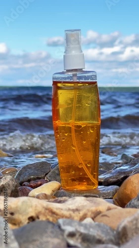 Close view of tanning lotion bottle on stones near sea water under bright summer sky. Concept: care and protection of skin under sun rays on the shore.