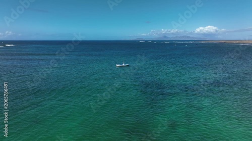 A drone view of a small boat sailing on crystal-clear waters in the Canary Islands