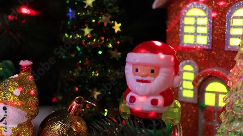 A close-up of a snowman with a yellow ball and Santa Claus on a sleigh in front of the houses